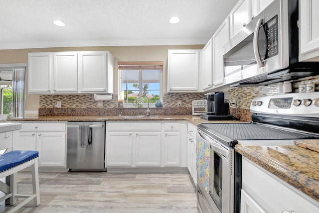kitchen featuring decorative backsplash, light stone counters, stainless steel appliances, white cabinetry, and a sink