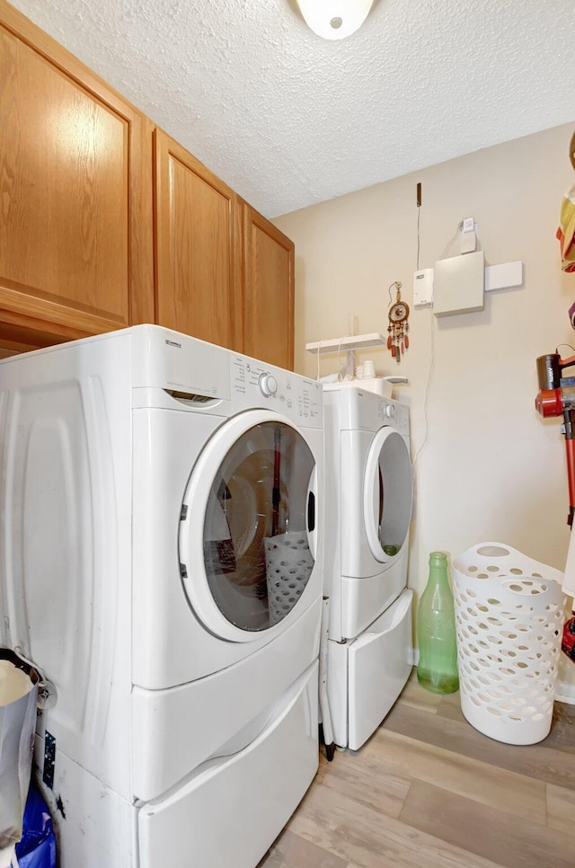 clothes washing area with cabinet space, light wood-style floors, separate washer and dryer, and a textured ceiling