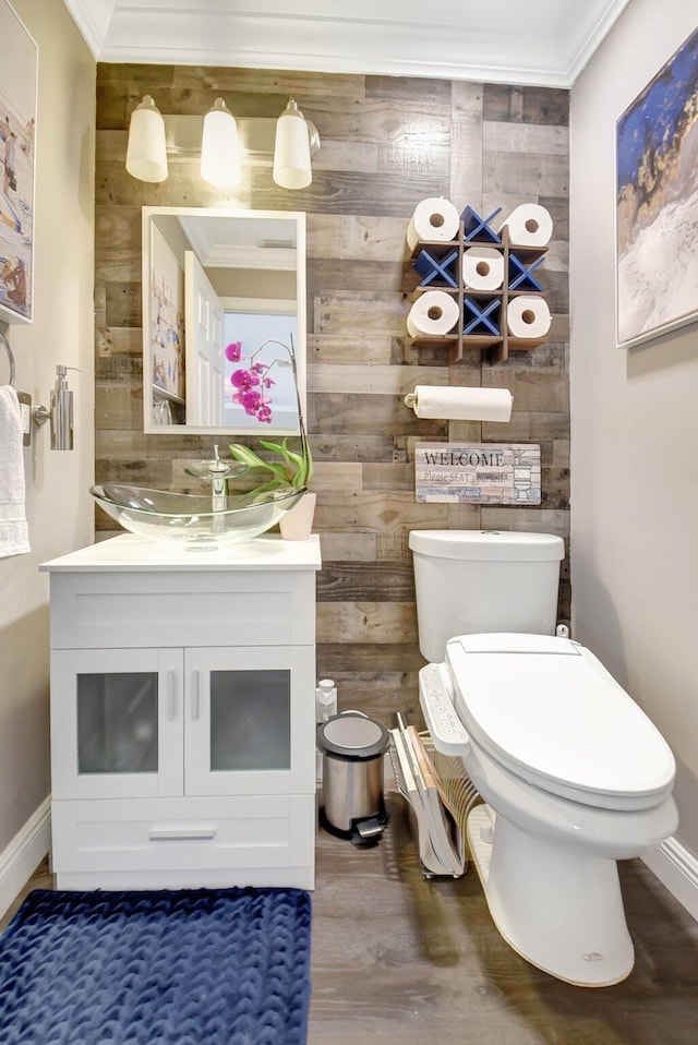 half bathroom featuring wooden walls, baseboards, toilet, wood finished floors, and vanity