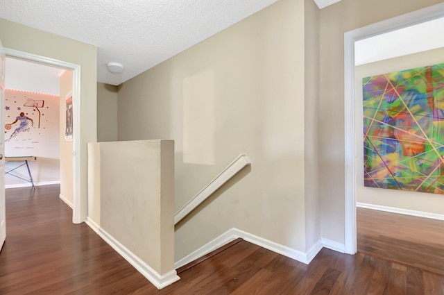 hall with dark wood-type flooring, baseboards, a textured ceiling, and an upstairs landing
