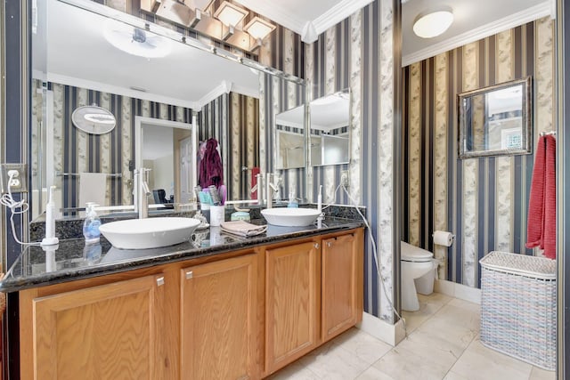 bathroom featuring double vanity, wallpapered walls, toilet, crown molding, and a sink