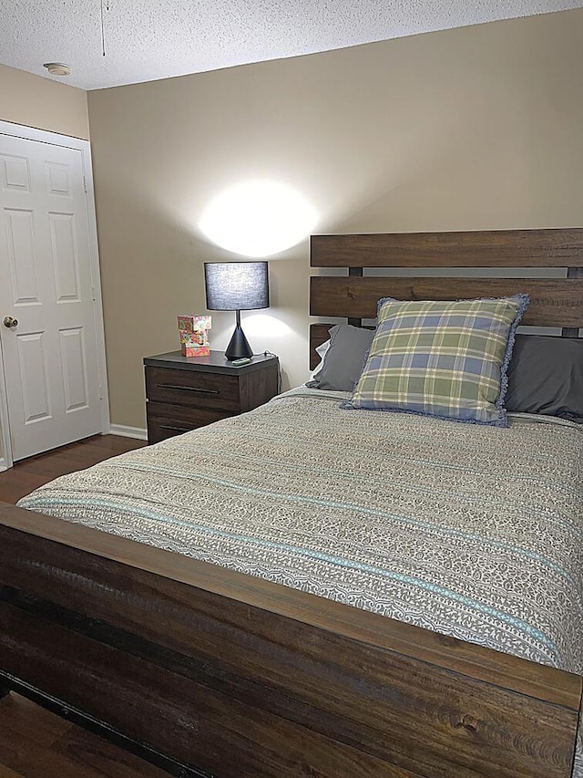 bedroom featuring baseboards, dark wood-type flooring, and a textured ceiling
