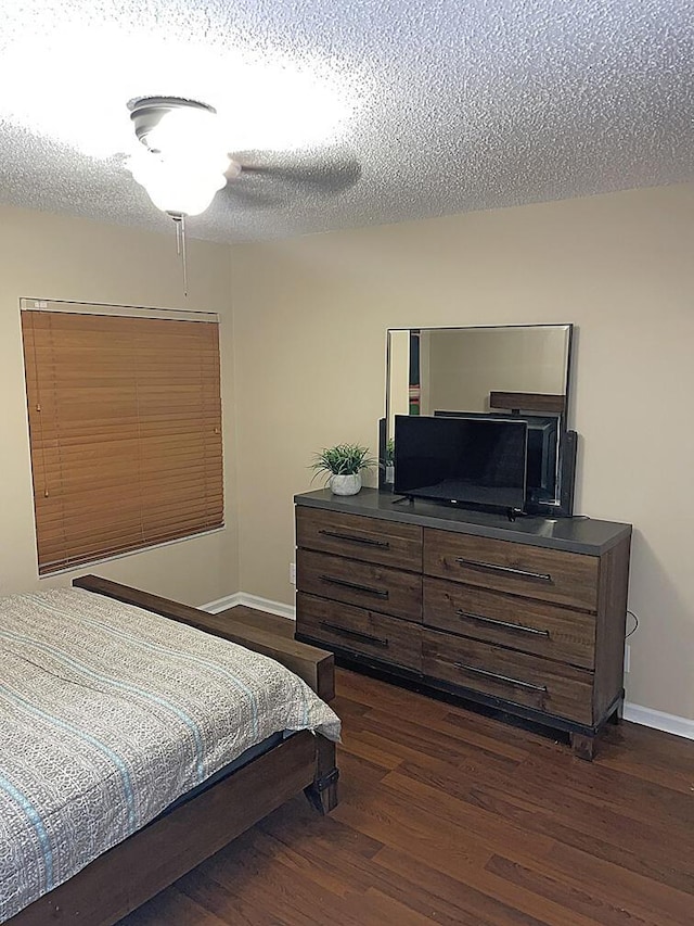 bedroom with a textured ceiling, dark wood finished floors, and baseboards