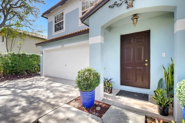 doorway to property with a garage, driveway, a tiled roof, and stucco siding