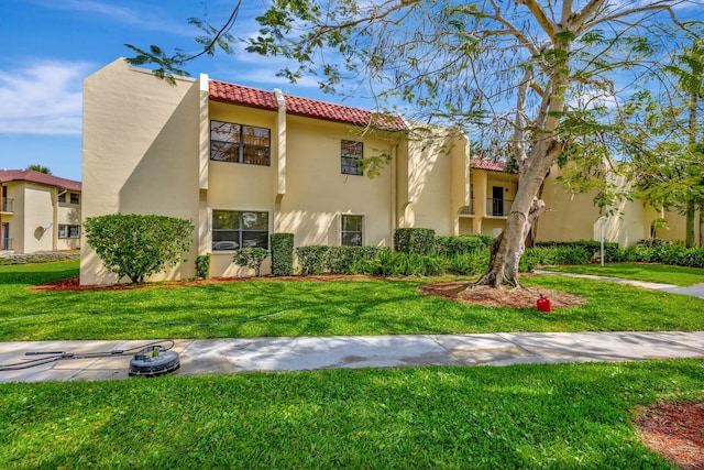 view of front facade featuring a tiled roof, a front lawn, and stucco siding