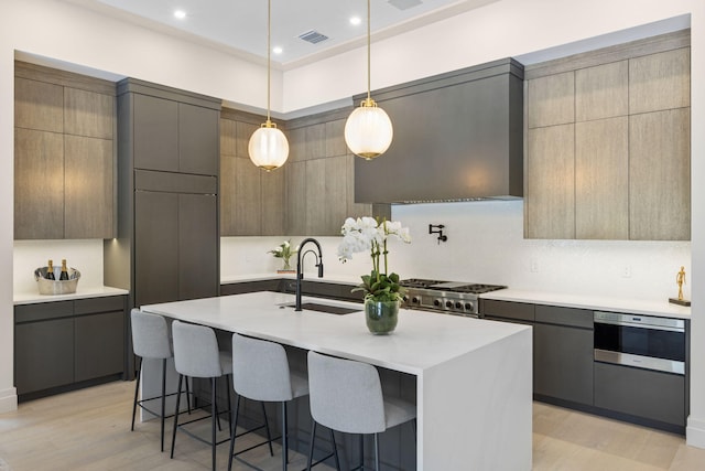 kitchen with light hardwood / wood-style flooring, an island with sink, decorative backsplash, pendant lighting, and sink