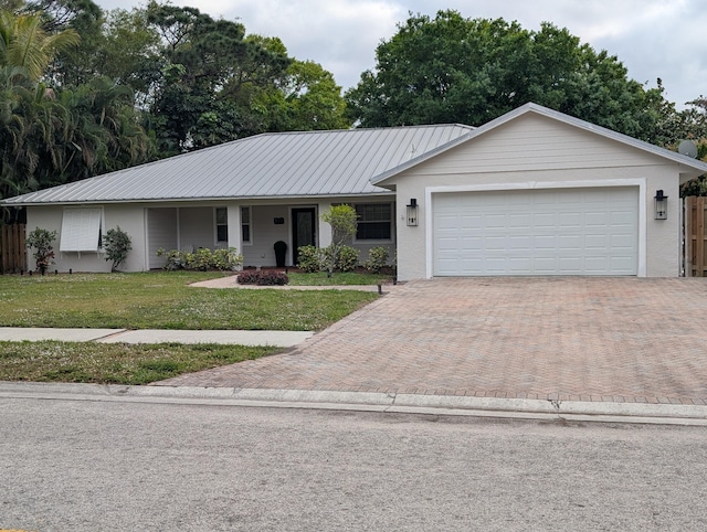 ranch-style house with metal roof, an attached garage, fence, decorative driveway, and a front lawn