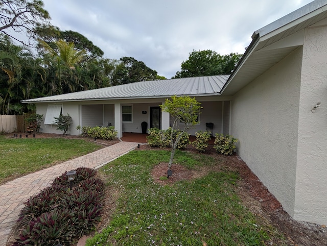 doorway to property with metal roof, covered porch, fence, a yard, and stucco siding