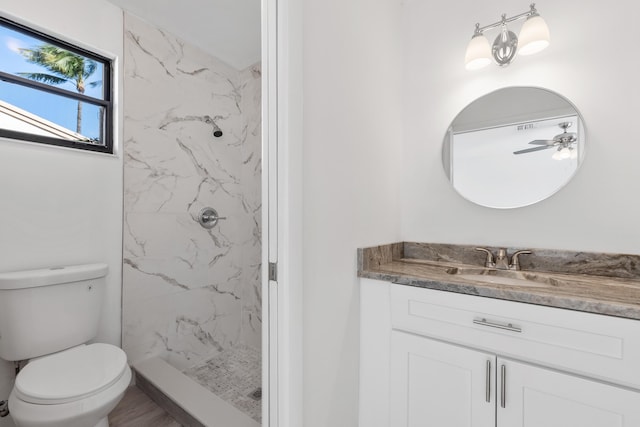 bathroom with ceiling fan, a tile shower, vanity, and toilet