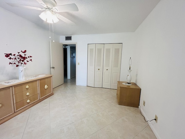 bedroom featuring visible vents, a ceiling fan, a textured ceiling, a closet, and light tile patterned flooring