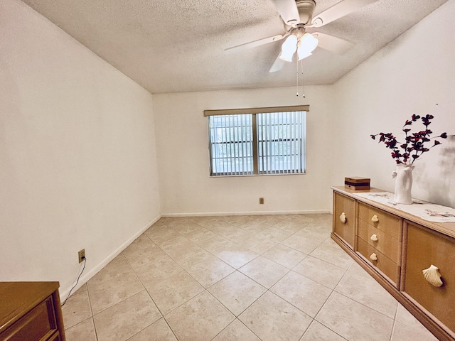 unfurnished room featuring a textured ceiling, ceiling fan, light tile patterned floors, and baseboards