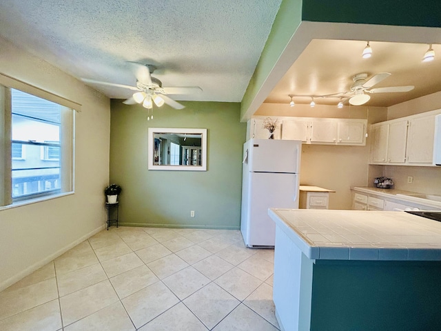 kitchen with tile counters, a ceiling fan, freestanding refrigerator, white cabinets, and a textured ceiling