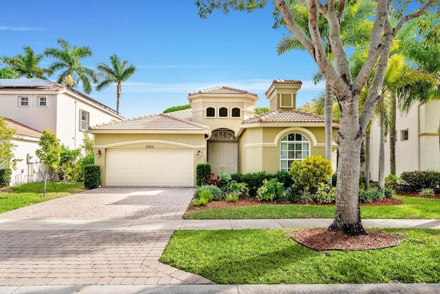 mediterranean / spanish house with stucco siding, a front lawn, a tile roof, decorative driveway, and an attached garage