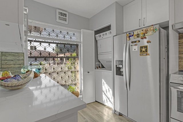 kitchen with appliances with stainless steel finishes, light stone counters, light wood-type flooring, stacked washing maching and dryer, and white cabinetry