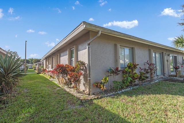 view of side of home featuring a yard, central air condition unit, and stucco siding