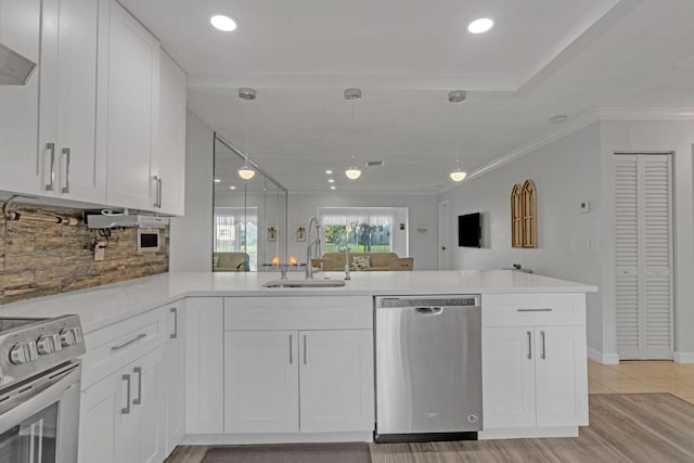 kitchen with light countertops, appliances with stainless steel finishes, white cabinets, a sink, and a peninsula