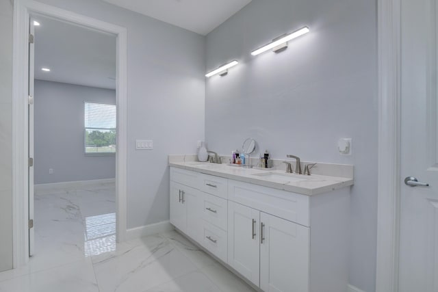 full bath featuring marble finish floor, a sink, baseboards, and double vanity