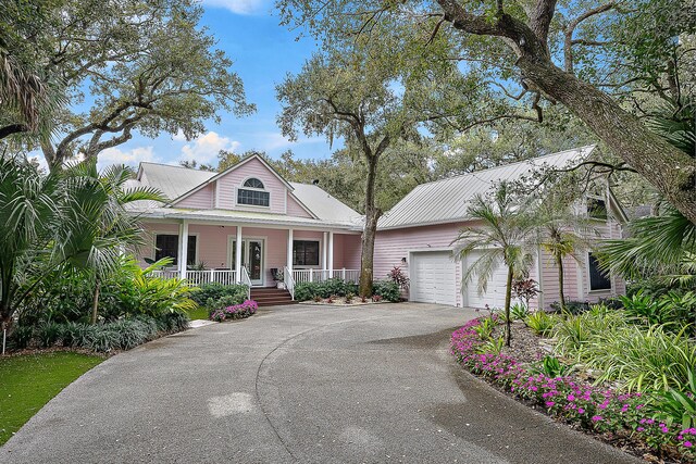 view of front facade with metal roof, an attached garage, a porch, and driveway