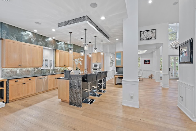 kitchen with light brown cabinetry, light wood-style floors, appliances with stainless steel finishes, dark countertops, and a kitchen breakfast bar