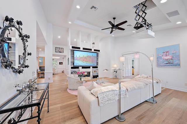 living area with light wood-type flooring, a tray ceiling, and a ceiling fan