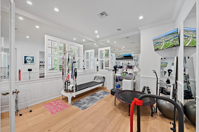 gym with visible vents, wood finished floors, crown molding, and a decorative wall