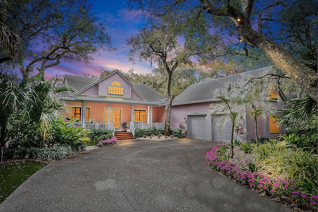 view of front facade featuring covered porch, driveway, metal roof, and a garage