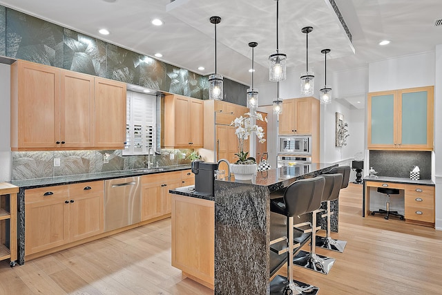 kitchen with a breakfast bar, an island with sink, light brown cabinetry, appliances with stainless steel finishes, and decorative backsplash