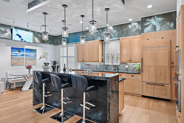 kitchen featuring a sink, built in appliances, light wood-style floors, and light brown cabinetry