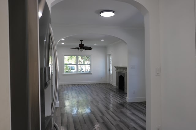 unfurnished living room with a fireplace with raised hearth, arched walkways, dark wood-type flooring, baseboards, and ornamental molding