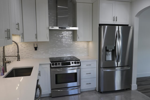 kitchen featuring light countertops, appliances with stainless steel finishes, white cabinets, a sink, and wall chimney exhaust hood