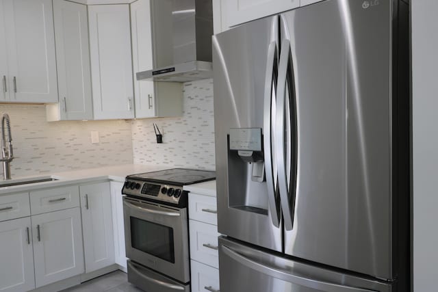 kitchen with appliances with stainless steel finishes, light countertops, wall chimney range hood, and white cabinetry