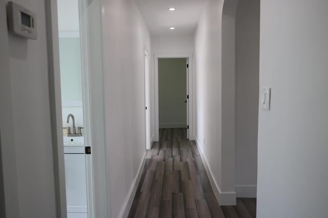 hallway featuring a sink, recessed lighting, dark wood finished floors, and baseboards