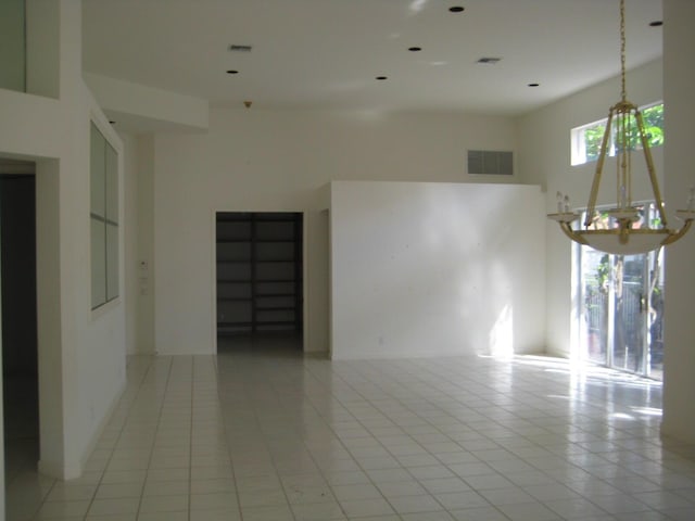 empty room featuring light tile patterned floors, a chandelier, and a towering ceiling