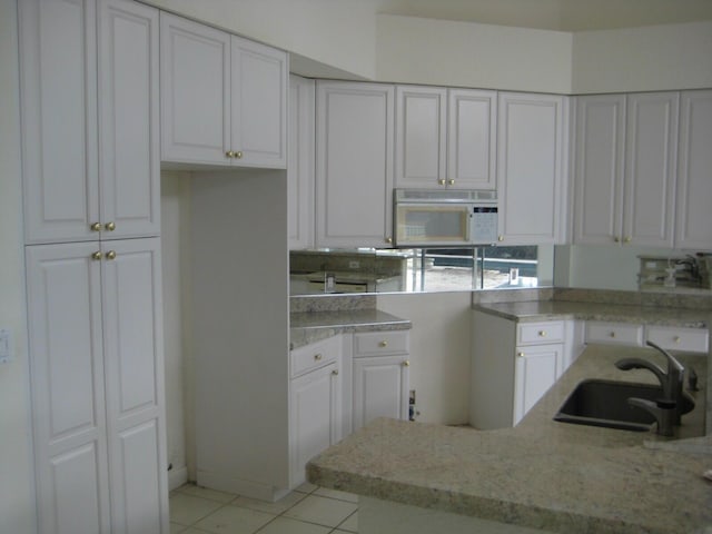 kitchen with sink, white cabinetry, light stone counters, and light tile patterned floors