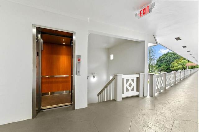 hallway featuring elevator, expansive windows, and an upstairs landing