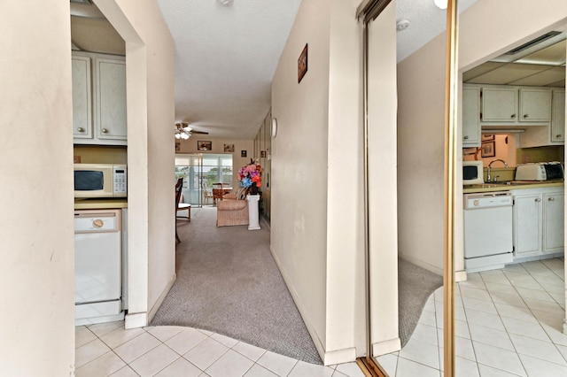 hall featuring light carpet, light tile patterned floors, visible vents, and a sink