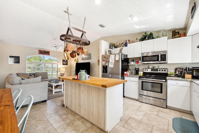 kitchen with wood counters, vaulted ceiling, a center island, white cabinetry, and stainless steel appliances