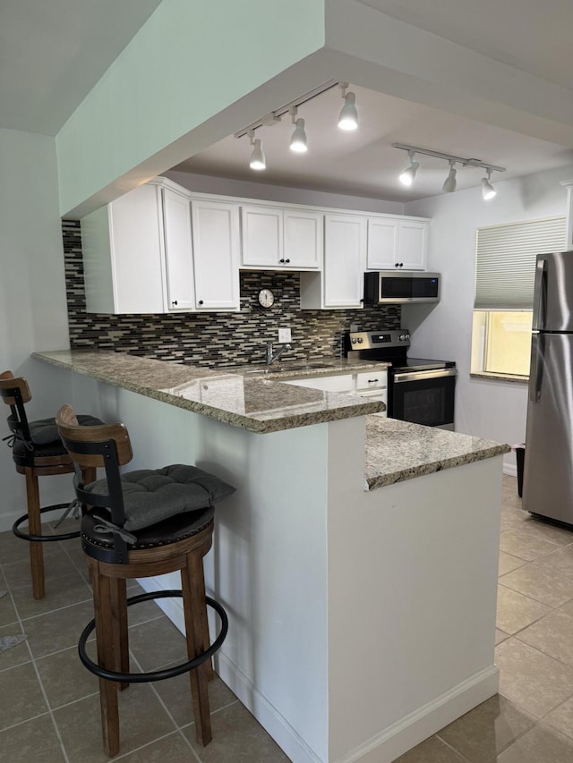 kitchen featuring stainless steel appliances, white cabinets, a peninsula, and light stone counters