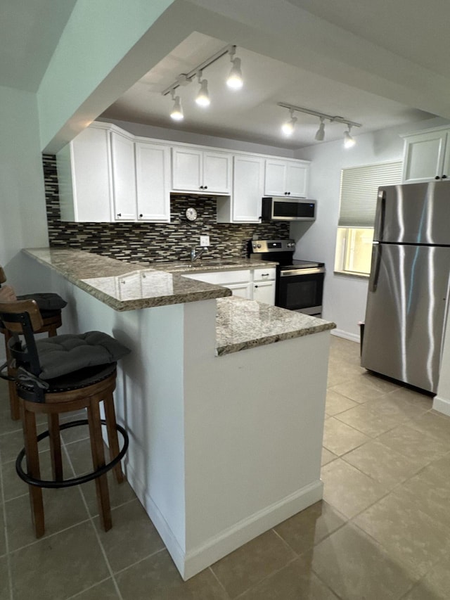 kitchen featuring stone countertops, appliances with stainless steel finishes, a peninsula, white cabinetry, and backsplash