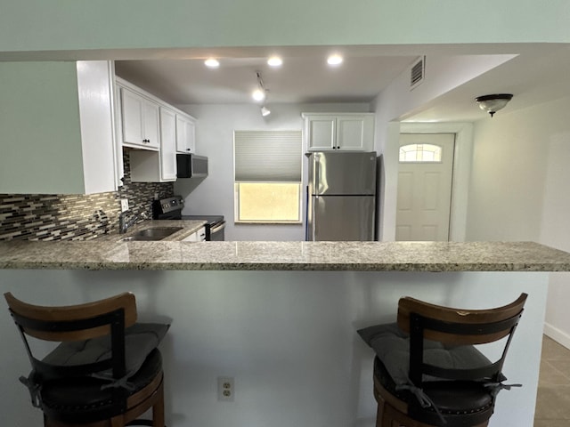 kitchen with light stone counters, a peninsula, visible vents, appliances with stainless steel finishes, and decorative backsplash