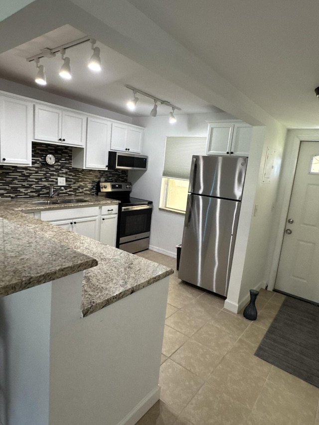 kitchen with light stone countertops, a sink, white cabinetry, appliances with stainless steel finishes, and decorative backsplash