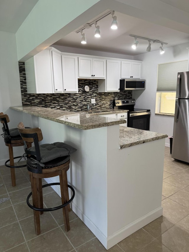 kitchen with stainless steel appliances, backsplash, white cabinetry, light stone countertops, and a peninsula