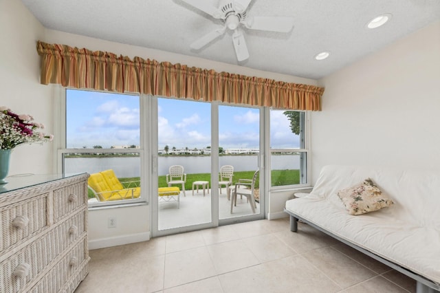 interior space with ceiling fan, a water view, light tile patterned flooring, and a textured ceiling