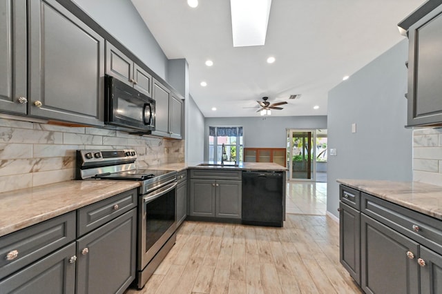 kitchen with gray cabinetry, a skylight, light wood-style floors, black appliances, and a sink