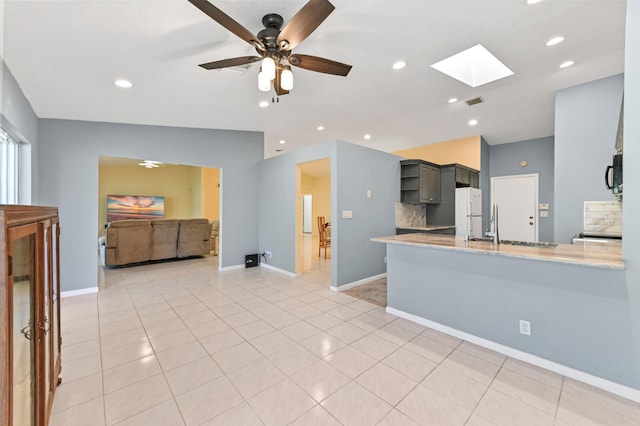 kitchen featuring light tile patterned floors, freestanding refrigerator, a sink, black microwave, and backsplash