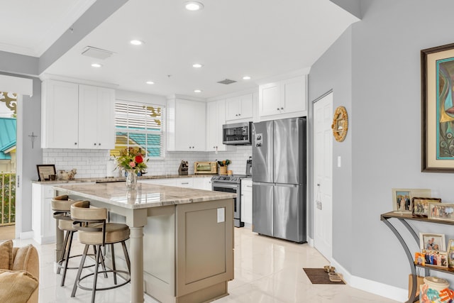 kitchen with stainless steel appliances, tasteful backsplash, white cabinetry, a kitchen island, and light stone countertops