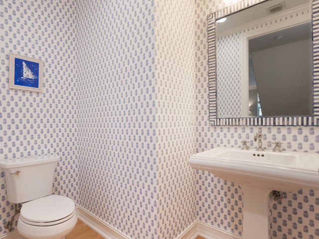 half bathroom featuring visible vents, toilet, and wallpapered walls