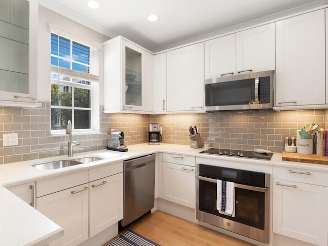 kitchen with stainless steel appliances, a sink, white cabinetry, light countertops, and glass insert cabinets