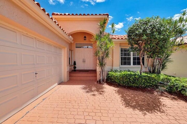 doorway to property featuring a garage, a tile roof, and stucco siding