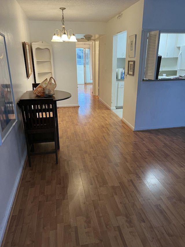 hallway with dark wood-style floors, baseboards, a textured ceiling, and an inviting chandelier